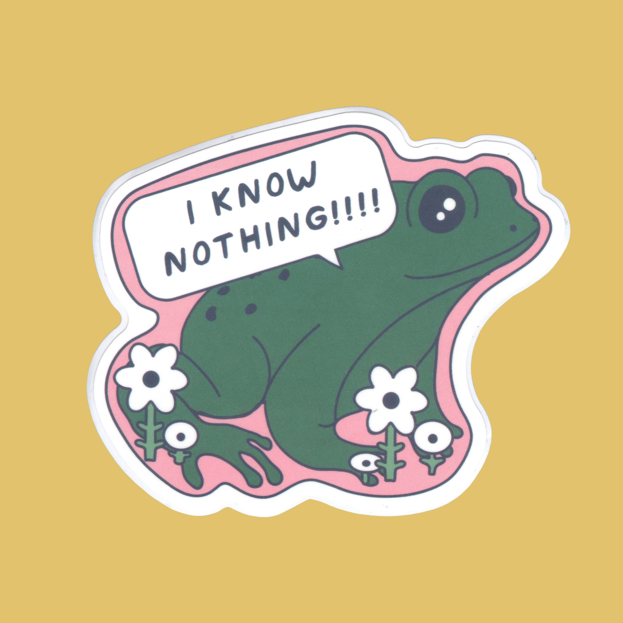 A die-cut sticker featuring a green cartoon frog sitting on pink grass with white flowers and a speech bubble that says 'I KNOW NOTHING!!!!', shown on a solid mustard yellow background.